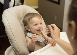 Infant wearing a bib being fed by his mother