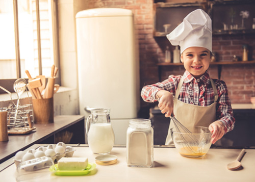 Kid wearing a chef hat whisking egg in a bowl.