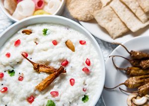 A bowl of curd rice garnished with pomegranate seeds, coriander leaves, cashews and fried chillies.