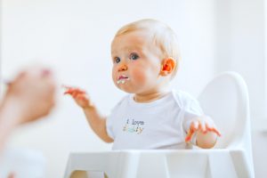 Baby in a high chair being fed solid food