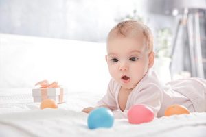 Cute baby with present and easter eggs lying on bed