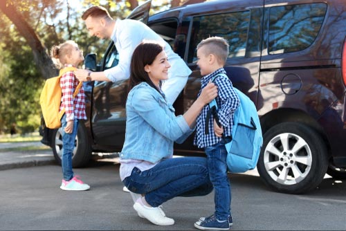 Parents standing by the car while they get their kids ready for school.