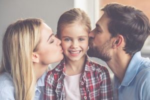 Mom and dad give their daughter a kiss on the cheek.