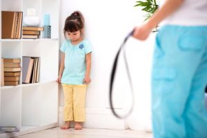 A child pushed to a corner as a parent holds a belt to punish her.