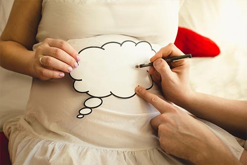 Man writing on a paper sign on pregnant wife's stomach