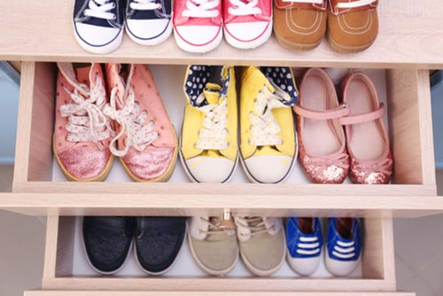 Different pairs of kids shoes places in a shoe rack.
