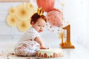 One-year-old baby eating cake with balloons in the background
