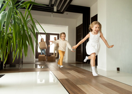 Kids running inside the house laughing while the parents smile and lift boxes behind them