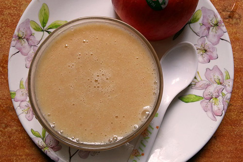 A plate with a bowl of oatmeal porridge and an apple