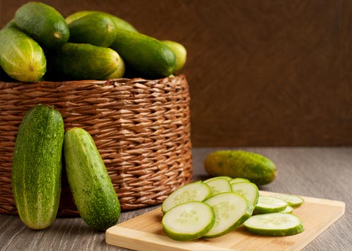 A basket of cucumbers next to a few cucumber slices.