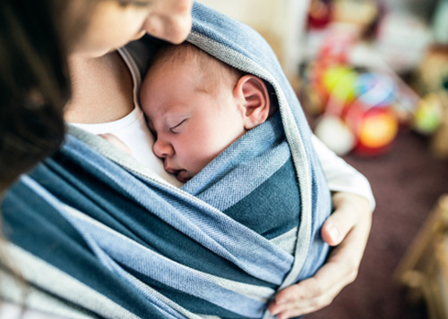 A mother soothing her baby in a shoulder sling.