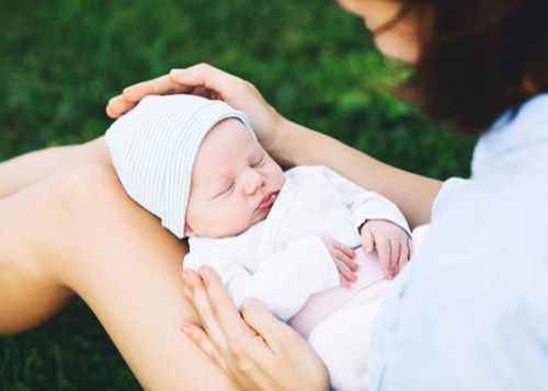 A mother seated outdoors with her baby fast asleep.