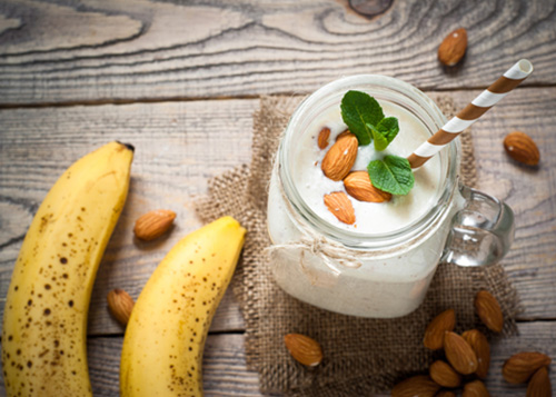 Banana and nut smoothie in a jar placed between bananas and almonds.