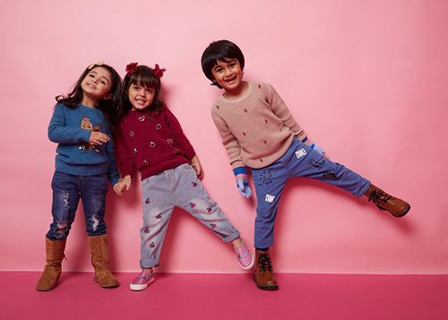Three kids dressed in denim pants and fancy sweaters.