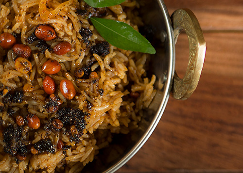 A serving bowl filled with tamarind rice garnished with groundnuts, curry leaves, and fried mustard seeds.