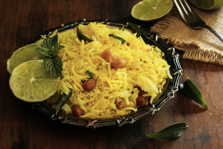 A bowl of lemon rice garnished with vegetables and a slice of lemon.