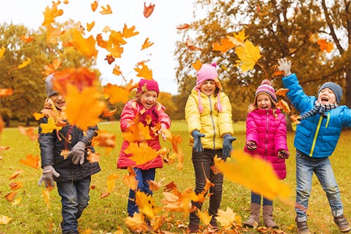 Kids dressed in autumn outfits playing in the park while leaves fall down