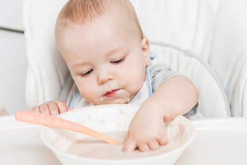 Baby dipping its finger in a bowl of cereal