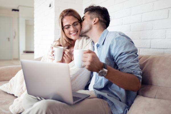 Couple sitting on a couch with a laptop and holding coffee mugs