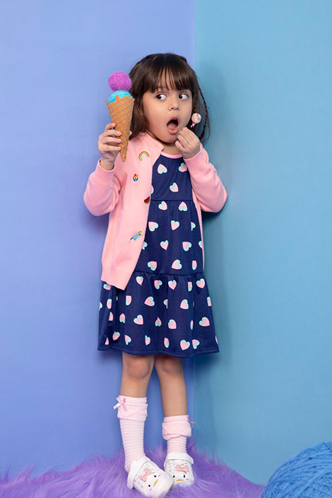 A girl wearing a blue printed dress and pink cardigan holding a fake ice cream cone