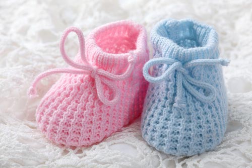 Pink crochet baby booties placed on top of baby clothes