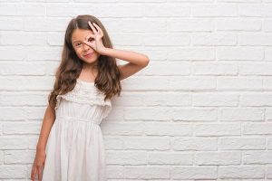 Adorable young girl in a white dress standing against a white brick wall!