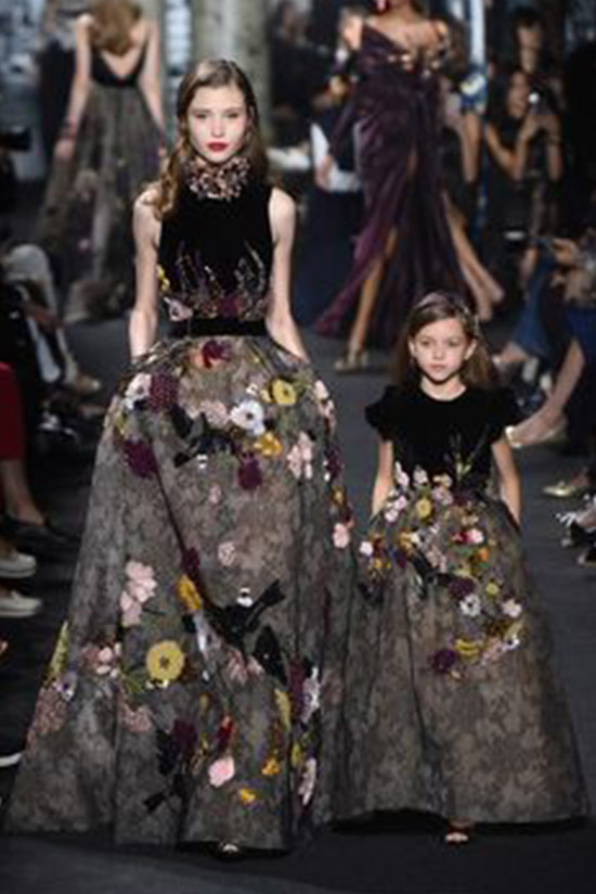A model and a younger model wearing similar gowns and walking down the ramp