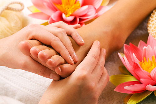 Picture of hands massaging a foot with flowers lying around the foot