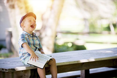 Little boy reading a book and laughing