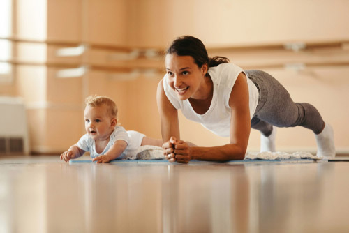 Mom doing a plank with a baby next to her