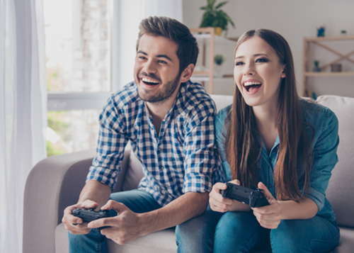Couple sitting on the couch and laughing with gaming controllers in their hand