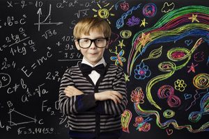 A young boy standing in front of a black board filled with mathematical equations.