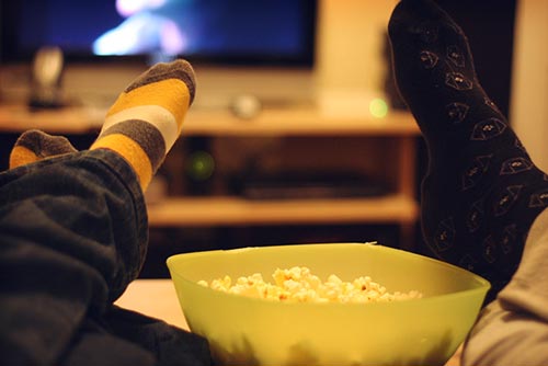 A child and parent watching a movie over popcorn.