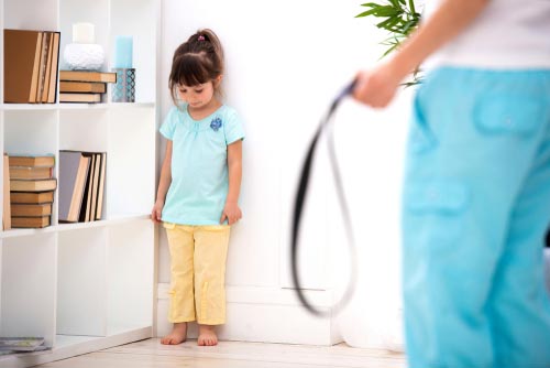 A child pushed to a corner as a parent holds a belt to punish her.