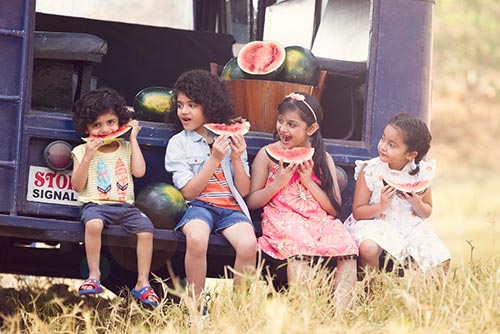 Kids sitting in the back of a jeep and eating watermelon.