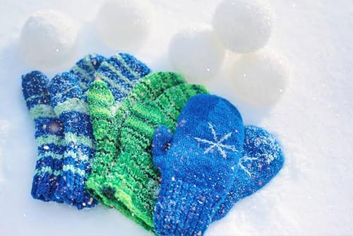 Blue and green kids winter mittens placed in the snow.