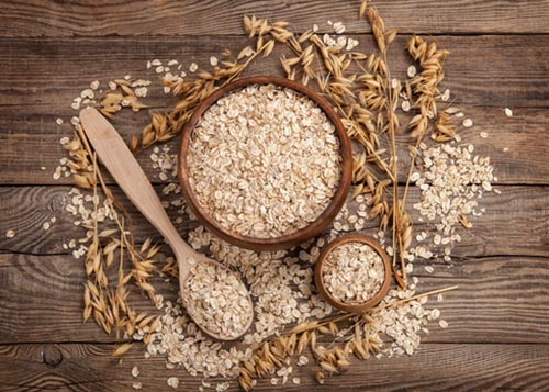 Wooden bowl and wooden spoon on a wooden table, all filled with oats and scattered with oat flakes