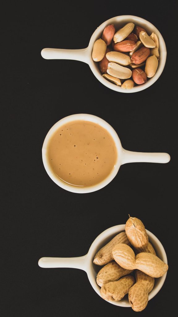 A bowl of shelled peanuts, a bowl of peanut butter, and a bowl of unshelled peanuts