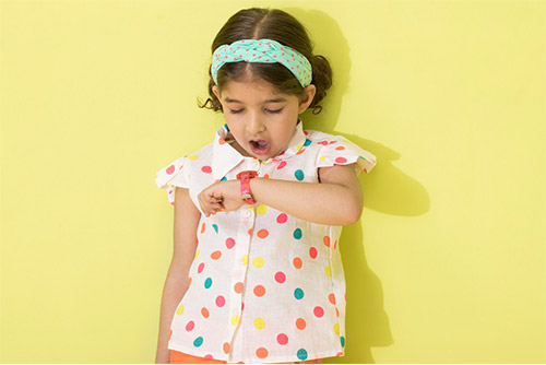 A girl wearing a polka dot top and headband looking in shock at her watch