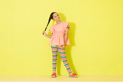 A girl twirling her braid wearing a coral top and colourful tights