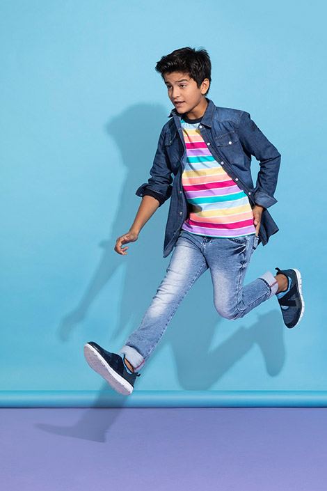 Picture of a boy jumping mid-air wearing a colourful tee, denim jacket, and jeans