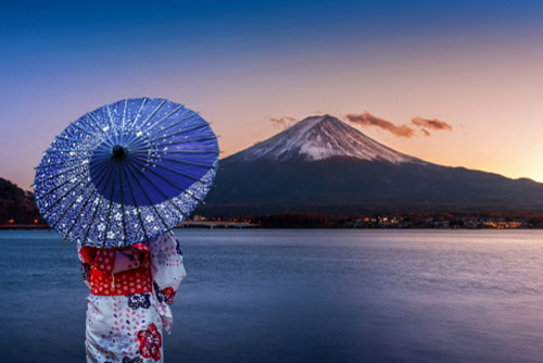 A Japanese lady with a beautiful blue umbrella admiring a mountain and a vast lake.