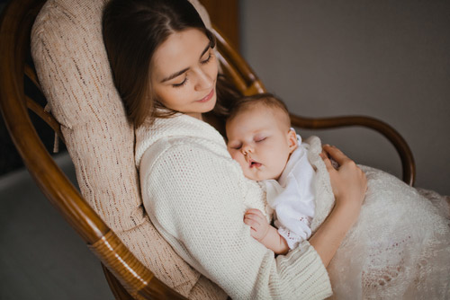 Mother holding a sleeping baby and sleeping on a chair