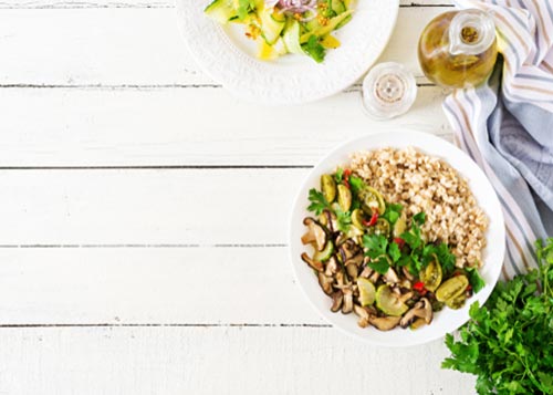 Bowl of oatmeal with vegetables with cilantro and olive oil next to it