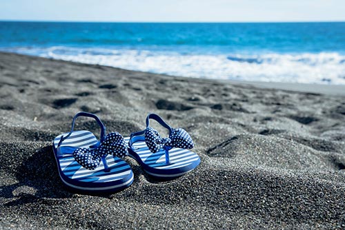 A pair of blue sandals with bows on a beach.