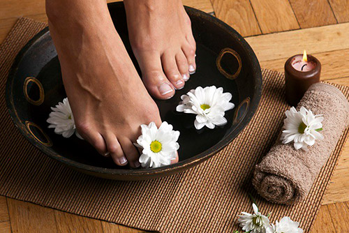 Picture of feet soaking in a bowl of water with flowers and a candle around the bowl