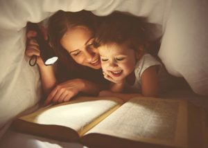 Adorable mother and daughter reading a book in torchlight