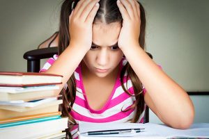 Stressed out young girl sitting on a chair with books piled up on a table!