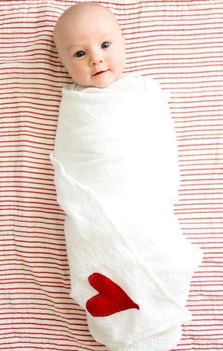 Baby swaddled in a white blanket lying against a red and white striped background