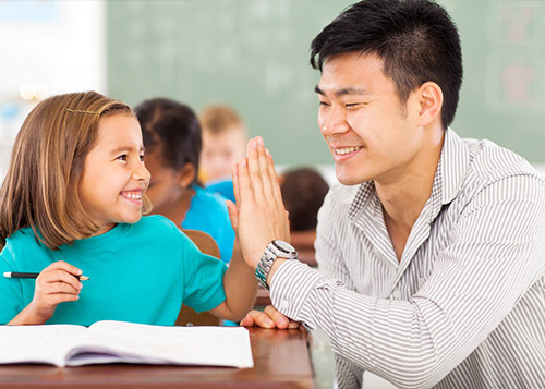 A school teacher gives a student a high-five.